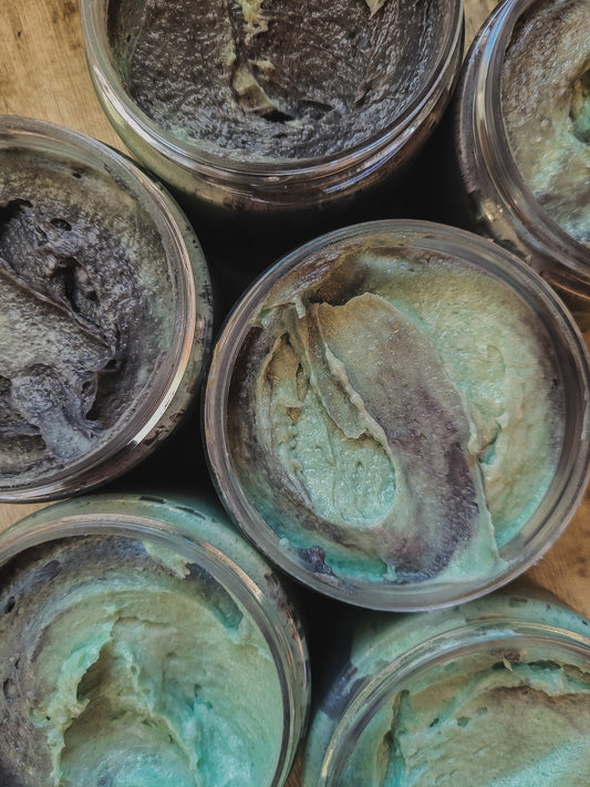 Jars of greenish-brown foaming scrub on a wooden surface