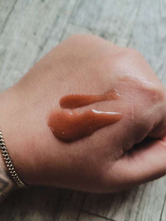 Hand with a small amount of lip gloss on a wooden surface