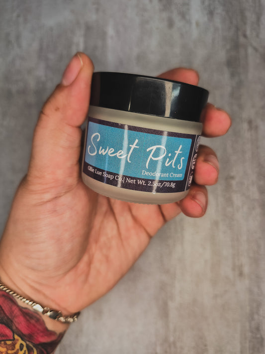 hand holding a jar of Sweet Pits deodorant cream on a gray background