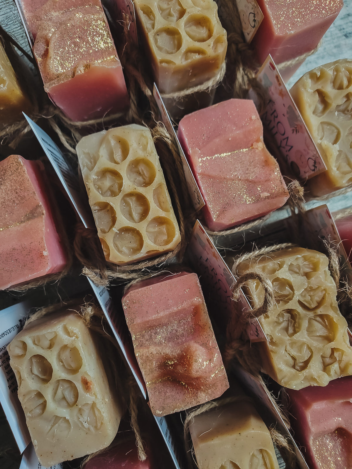 A close-up arrangement of handmade rectangular bars of soap tied with twine, showing pink and beige marbled soap with embossed circular and star patterns.