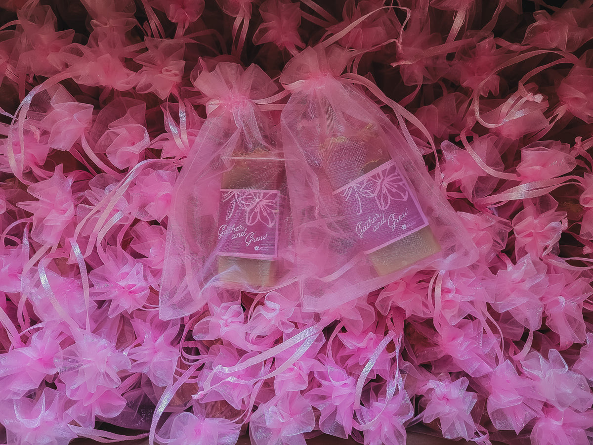 Two small soaps wrapped in sheer pink organza gift bags, placed on top of pink decorative paper flowers.