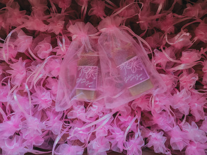Two small soaps wrapped in sheer pink organza gift bags, placed on top of pink decorative paper flowers.