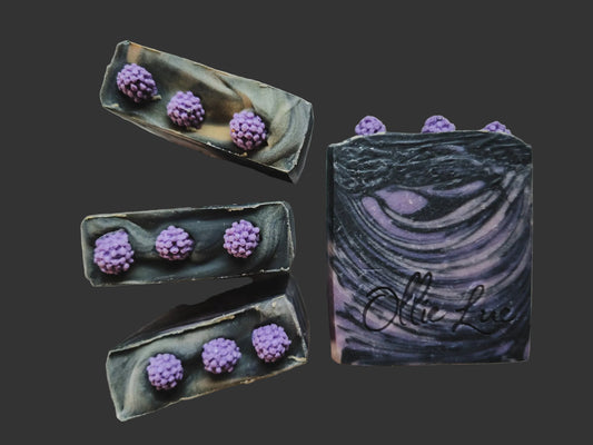 swirled black and purple soap with soap raspberry embeds on top all on a dark background