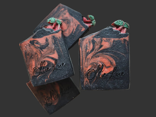 red and black swirled soap with a soap cherry on top stamped 'ollie lue' all on a dark background