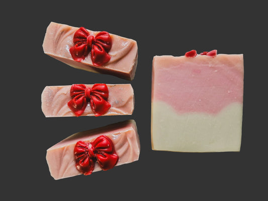 white cat style shape on the inside of the bar of soap with a pink layer on top that is topped with a red soap bow all on a dark background