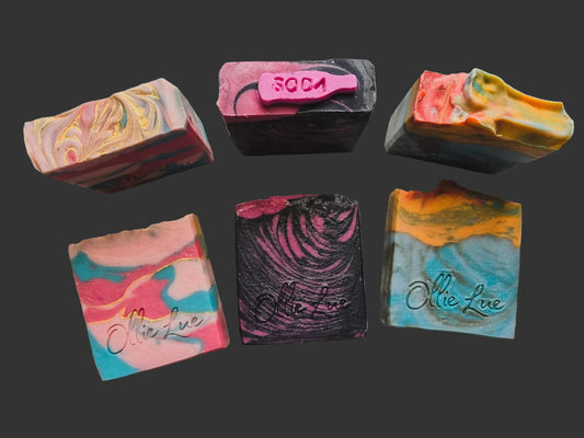a trio set of soap featuring a pink and blue bar, pink and black bar, and orange and blue bar all stamped ollie lue