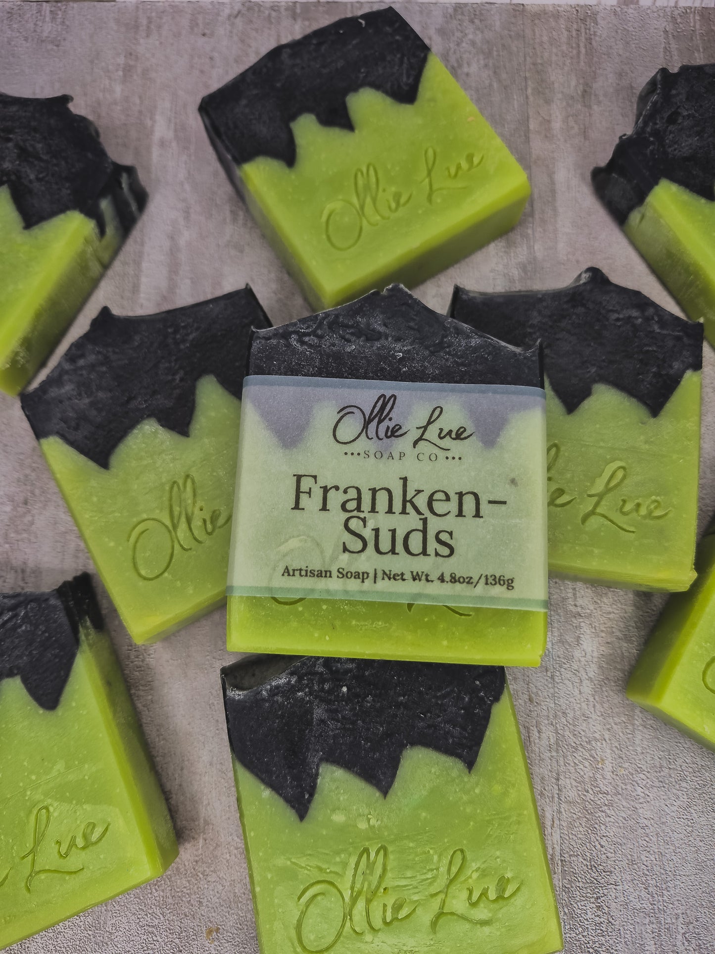 Several handmade soap bars with lime green bodies and black bat-wing shaped tops are arranged on a light textured surface. The center soap has a paper label reading 'Otte Lue Soap Co.