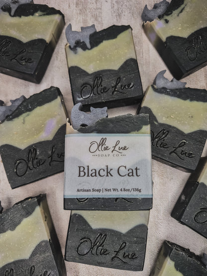 Several handmade soap bars are arranged on a light fabric background, with one central bar wrapped in a paper label that reads 'Olie Lue Soap Co