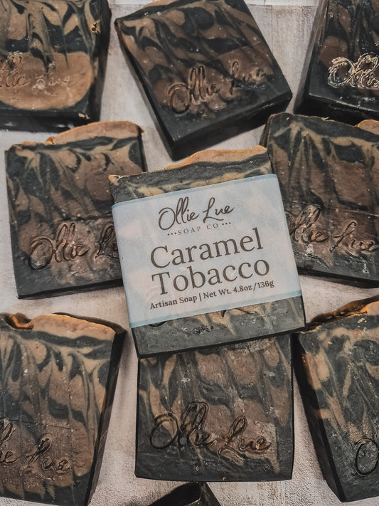 Several handmade soap bars are arranged on a light fabric background. The center soap is labeled 'Olle Lue Soap Co.