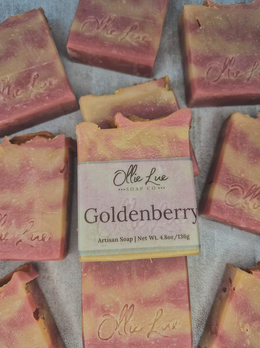 Artisan soap bars in a pink and golden-yellow marbled pattern, with a central bar wrapped in a paper label that reads 'Ollie Lue Soap Co. Goldenberry'.
