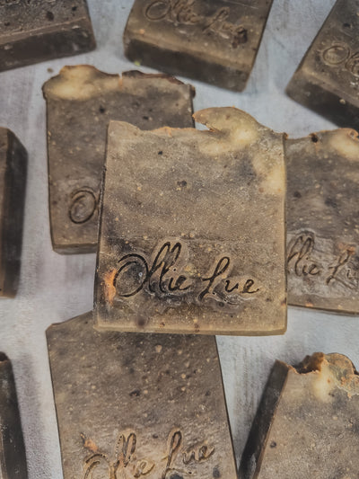 Several handmade rectangular bars of soap in a dark brown and beige marbled pattern, with the brand name 'ollie lue' embossed on the top, arranged on a light gray background.