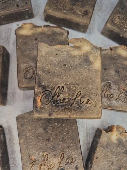 Several handmade rectangular bars of soap in a dark brown and beige marbled pattern, with the brand name 'ollie lue' embossed on the top, arranged on a light gray background.