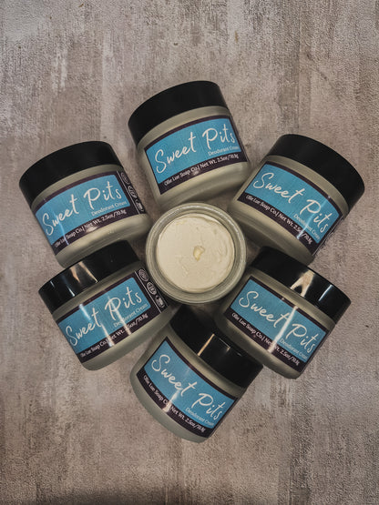 Six jars of Sweet Pits arranged in a circle on a textured gray surface, with one open jar in the center showing the creamy off-white oil.